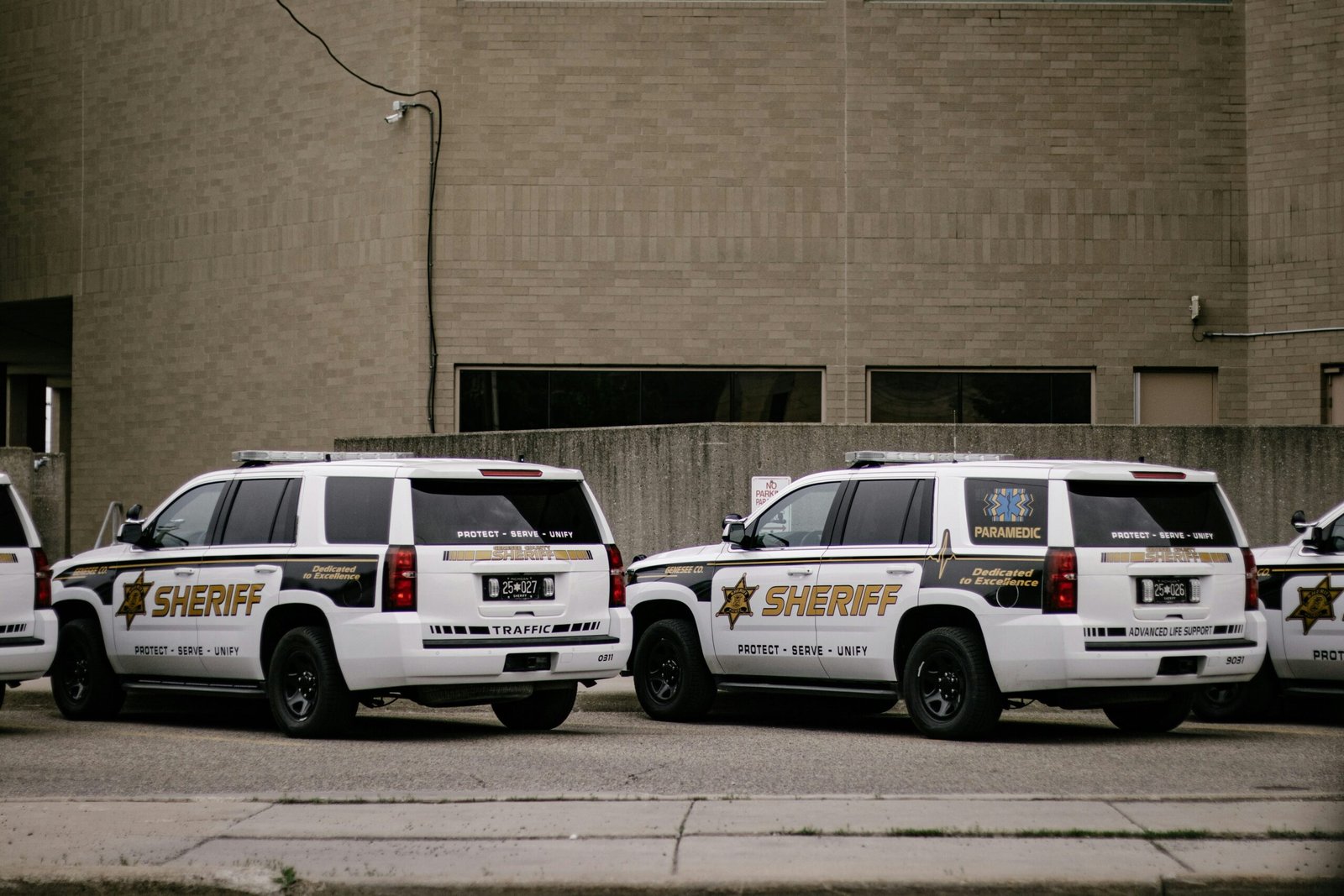 White law-enforcement vehicles parked outside a brick municipal building