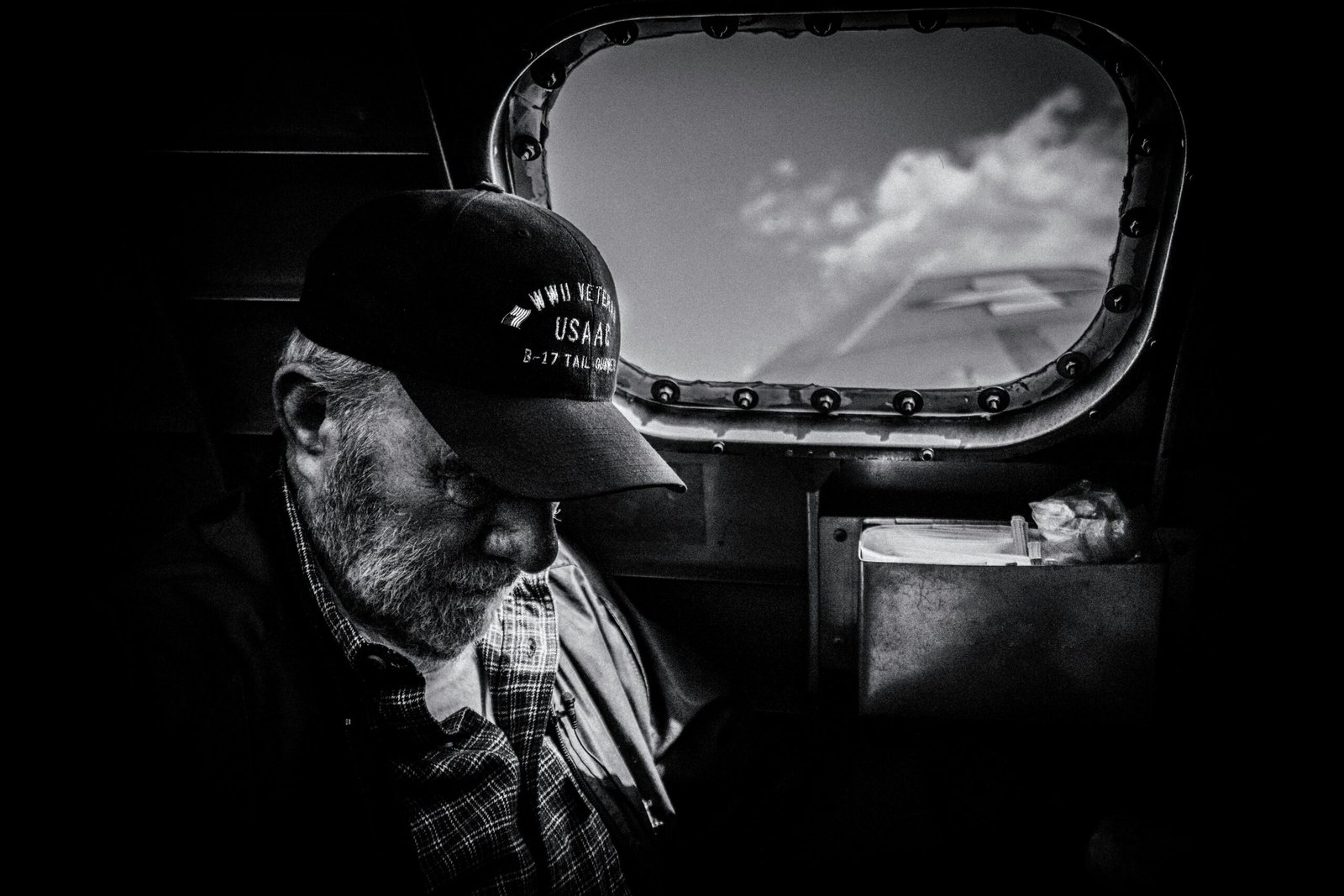 Black and white silhouette of a veteran wearing a cap with his head bowed against a bright window.