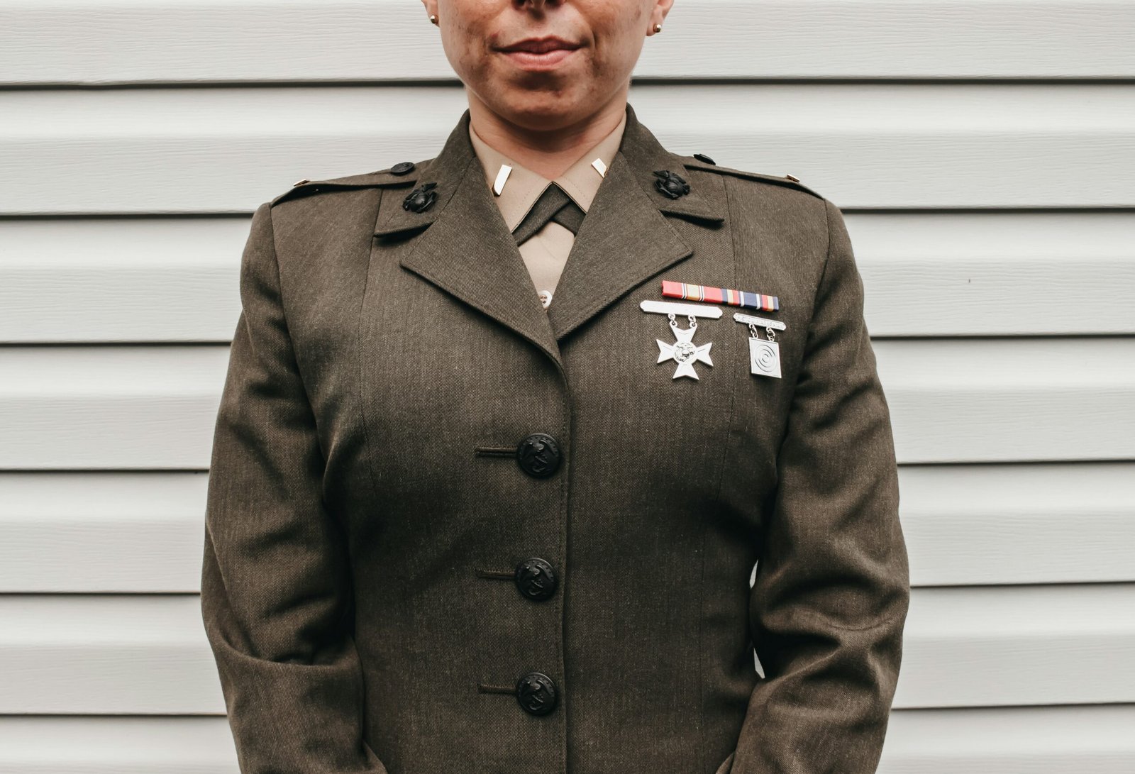 Close-up of a female military service member's torso wearing an olive green dress uniform with ribbons.