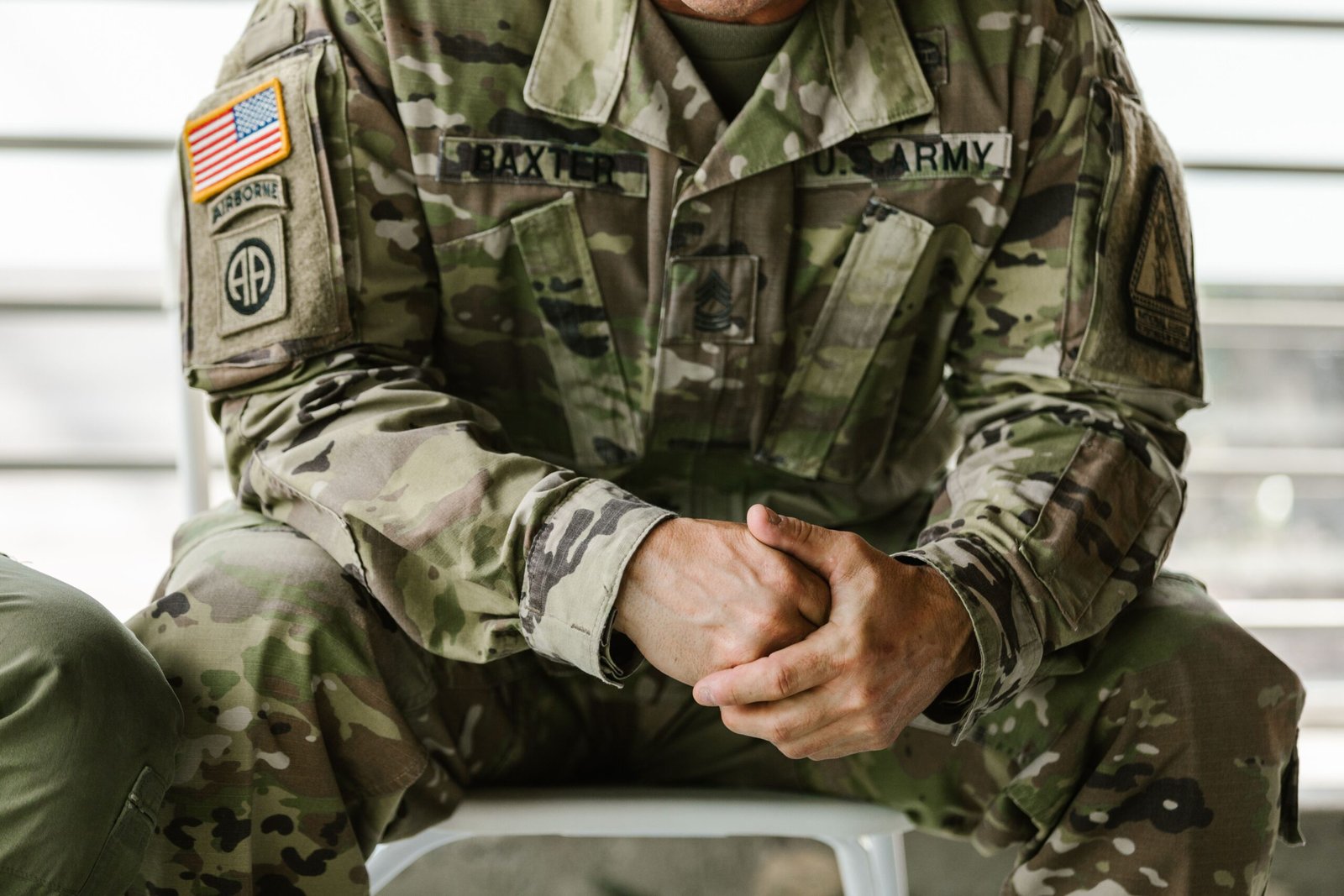 Close-up of a military service member's hands resting clasped in their lap over a camouflage uniform.