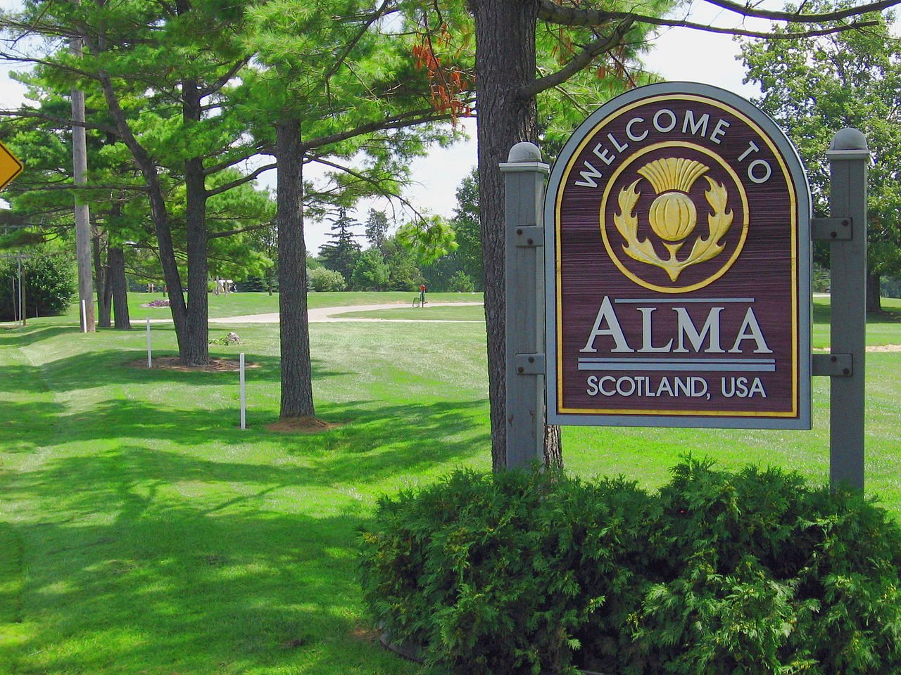 The Welcome to Alma sign on a tree-lined road at the edge of Alma, Michigan.