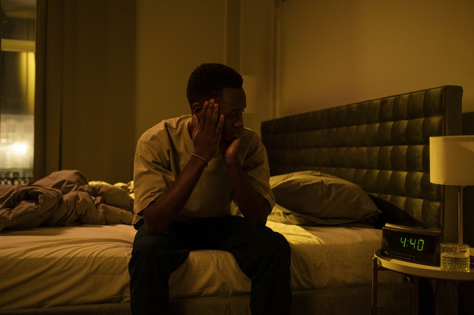A man sitting on the edge of his bed at night, unable to sleep.