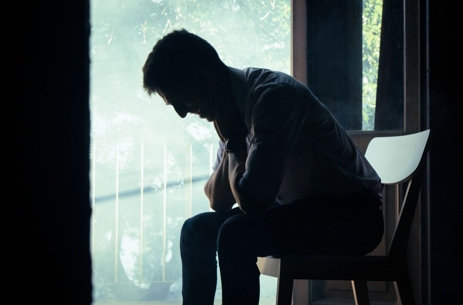 A person sitting alone in a dimly lit room, turned toward the light.